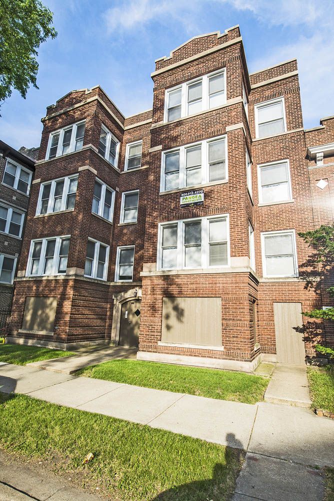 Brick apartment building with white-framed windows, green lawn, and sidewalk.