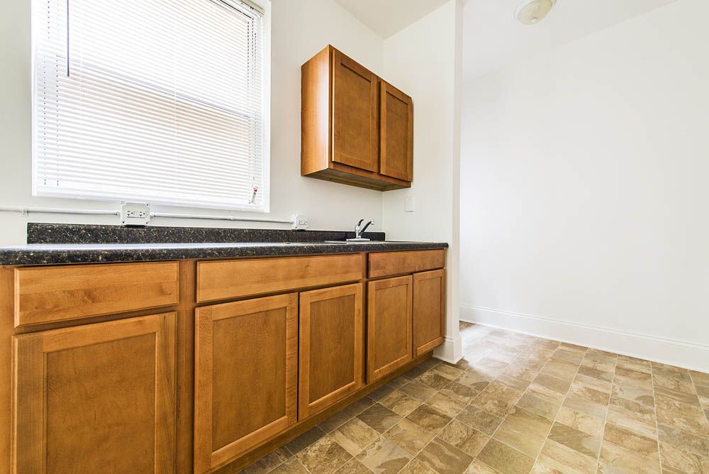 Kitchen with wooden cabinets, dark countertop, window, and vinyl flooring.