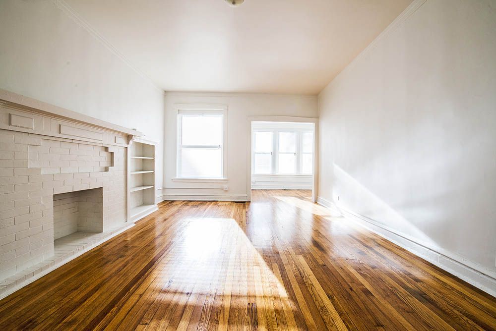 Empty room with hardwood floors, fireplace, two windows, and white walls.