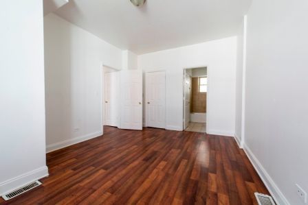 Empty room with dark wood flooring, white walls, and three white doors leading to other rooms.