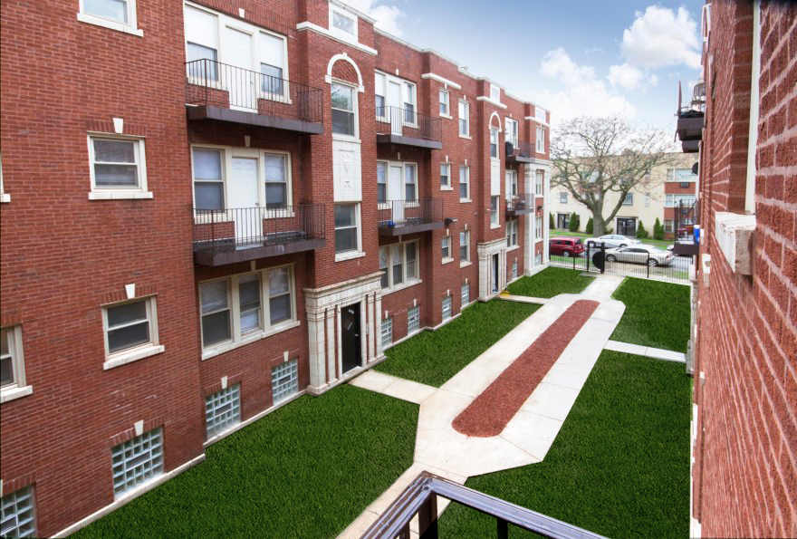 Red brick apartment building with courtyard and green lawn.