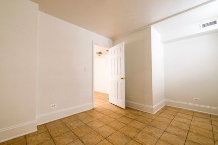 Empty room with tile floor, white walls, and a partially open door to another room.