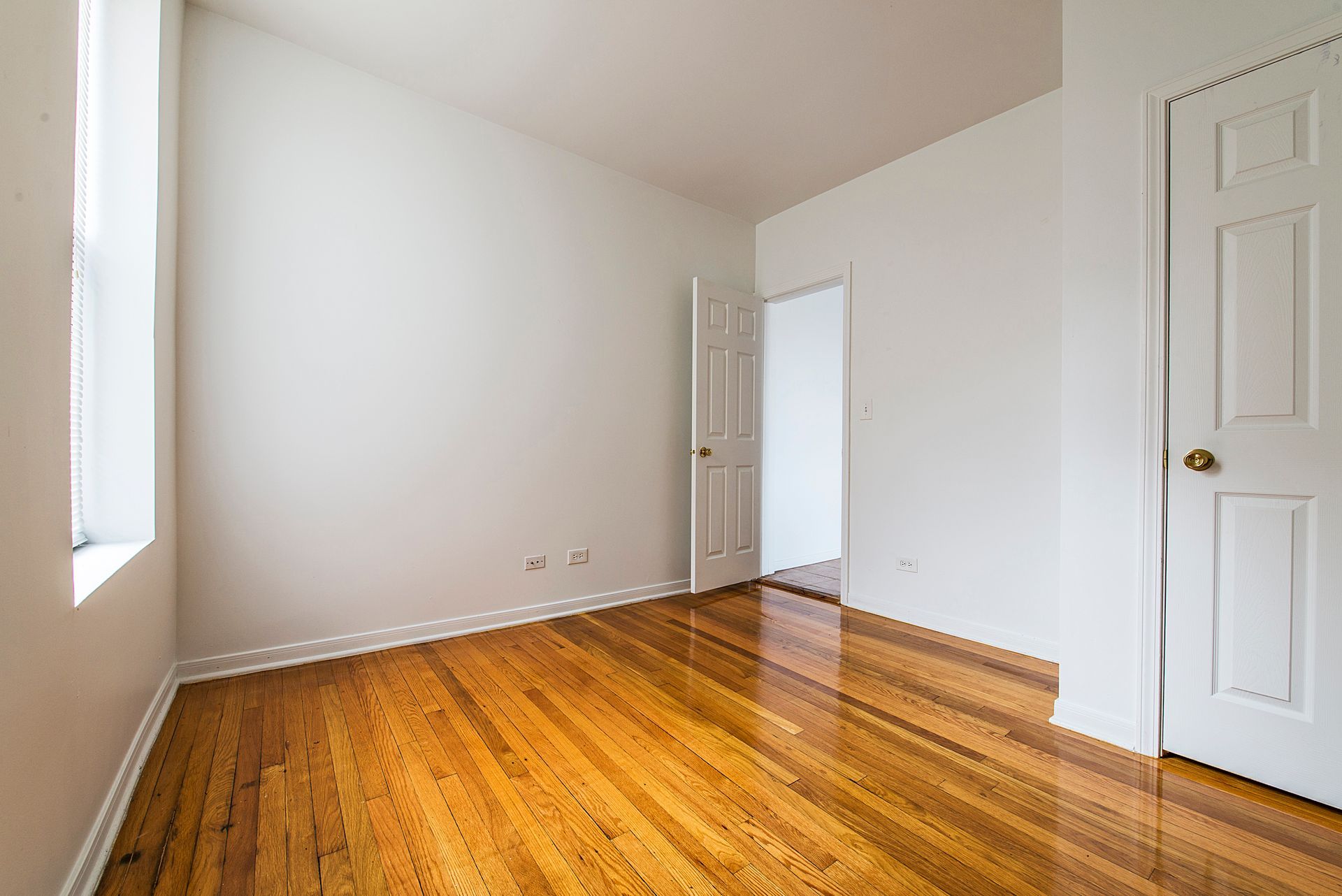 Empty room with hardwood floors, white walls, and two closed doors.