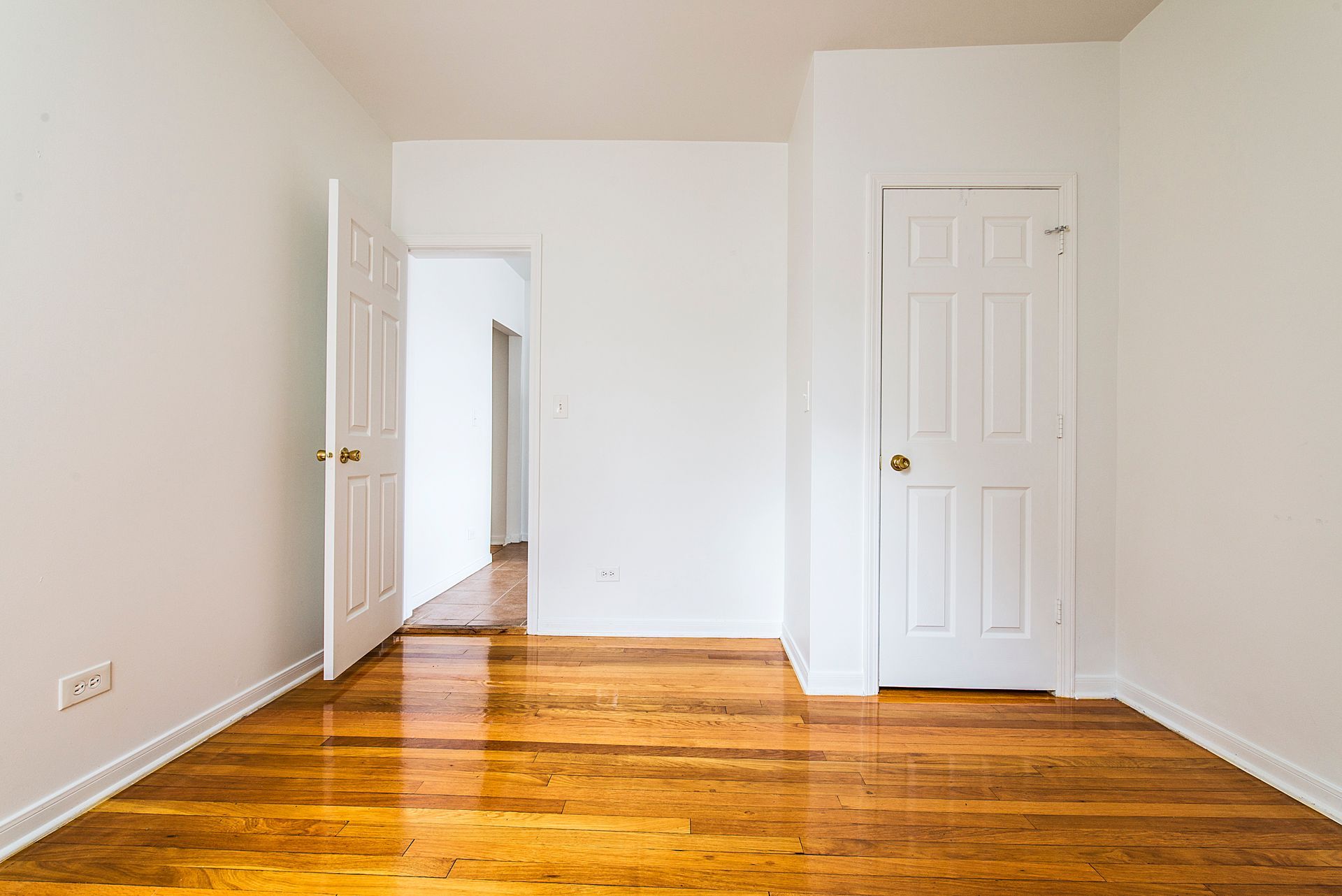 Empty room with hardwood floors, white walls, two closed doors, and one open doorway.
