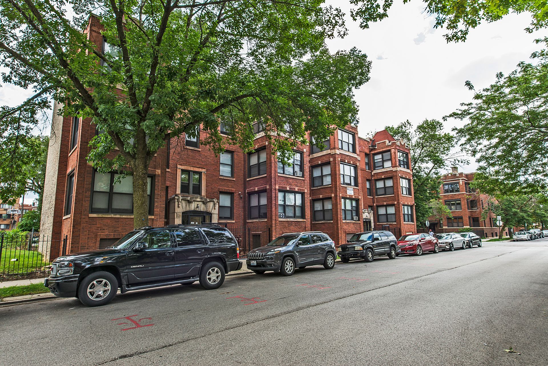 Row of brick apartment buildings with cars parked along the street.