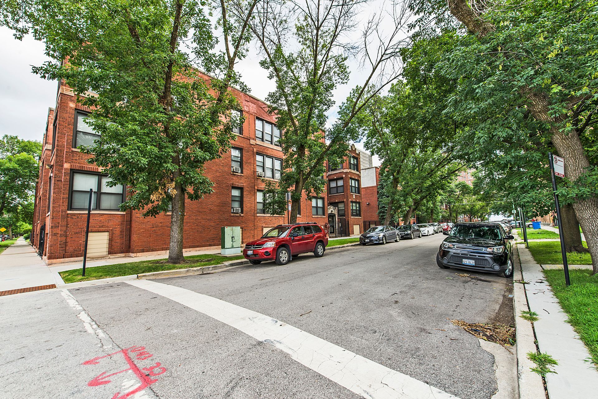 Red brick apartment building on a tree-lined street with parked cars.