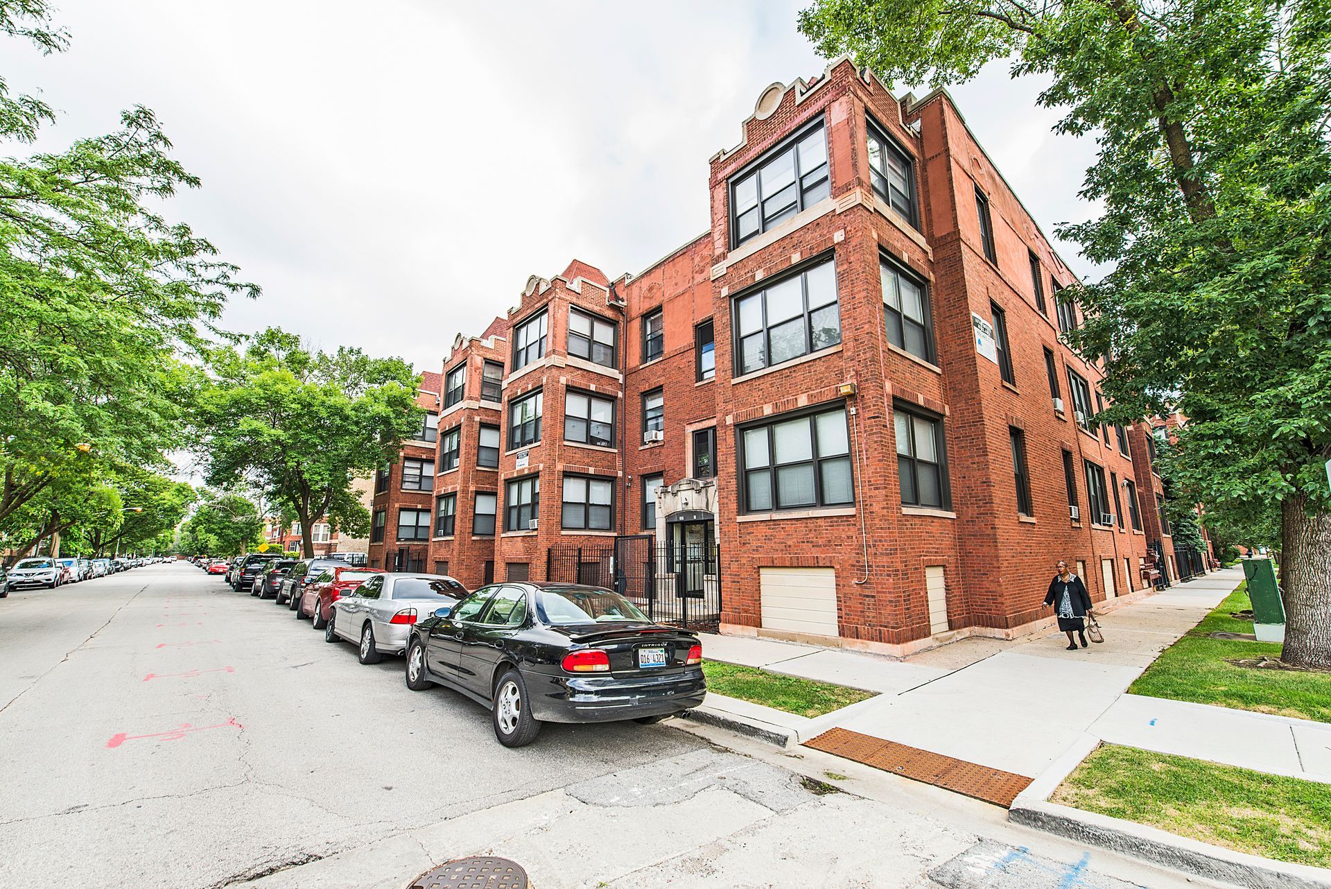 Red brick apartment building on a tree-lined street with parked cars.