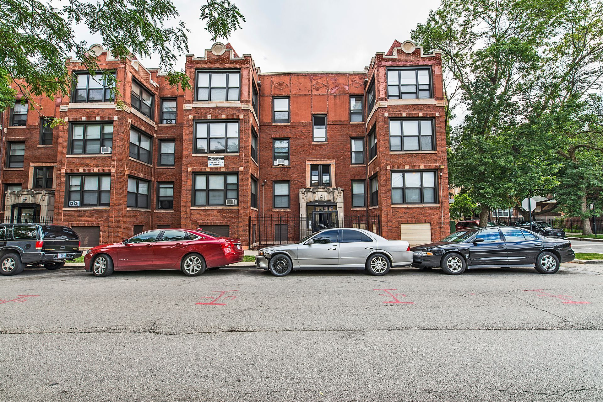 Apartment building with brick facade and parked cars on street.