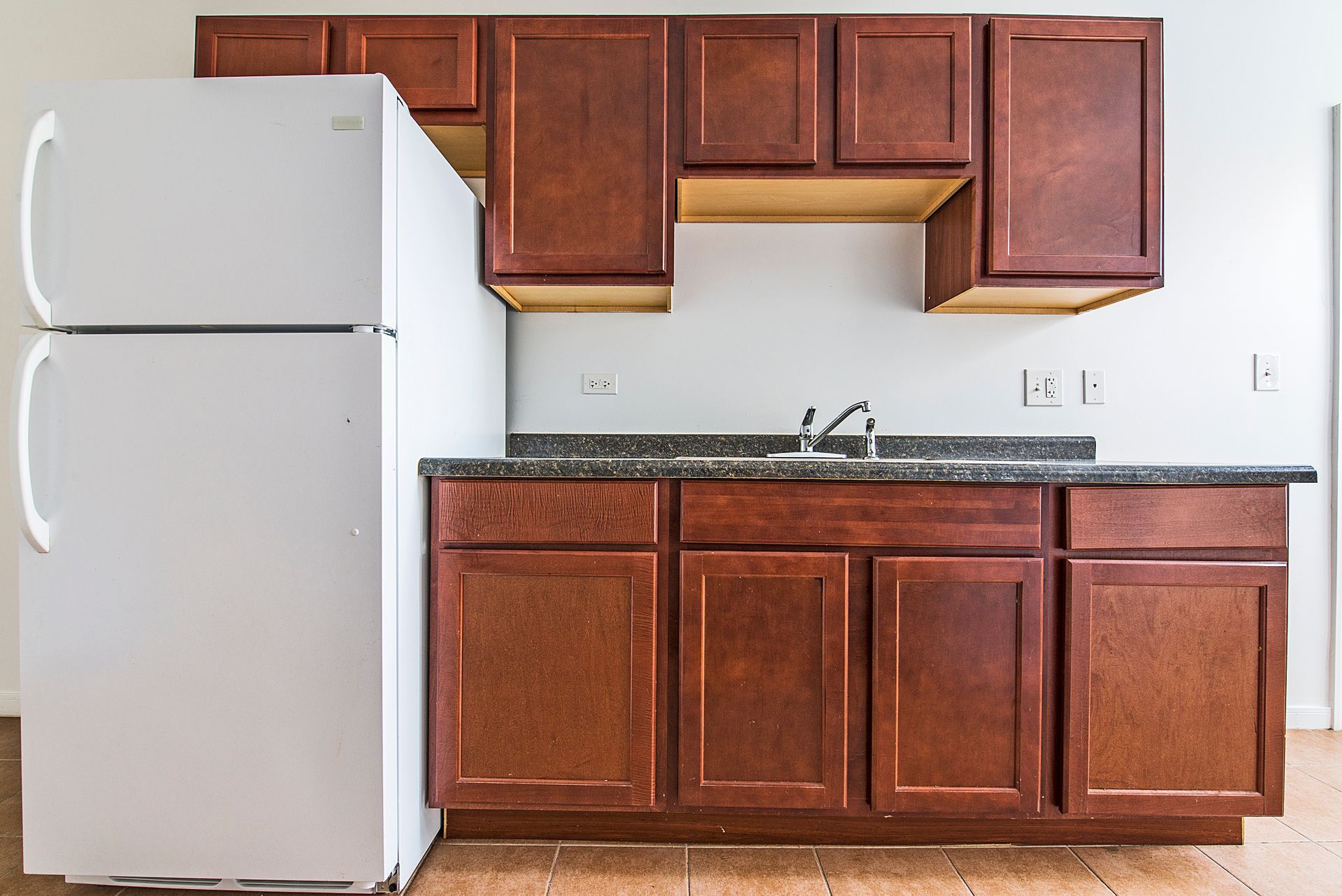 Kitchen with brown cabinets, white refrigerator, dark countertop, and silver sink.