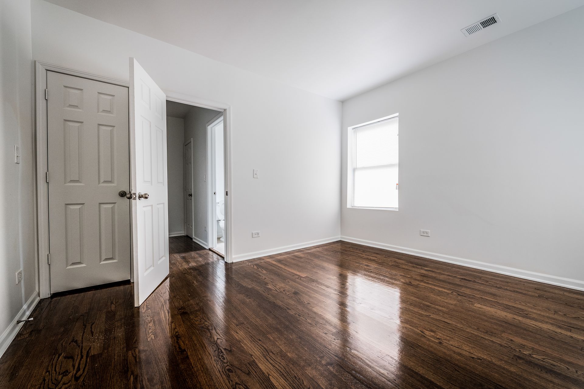 Empty room with hardwood floors, white walls, two open doors, and a window.