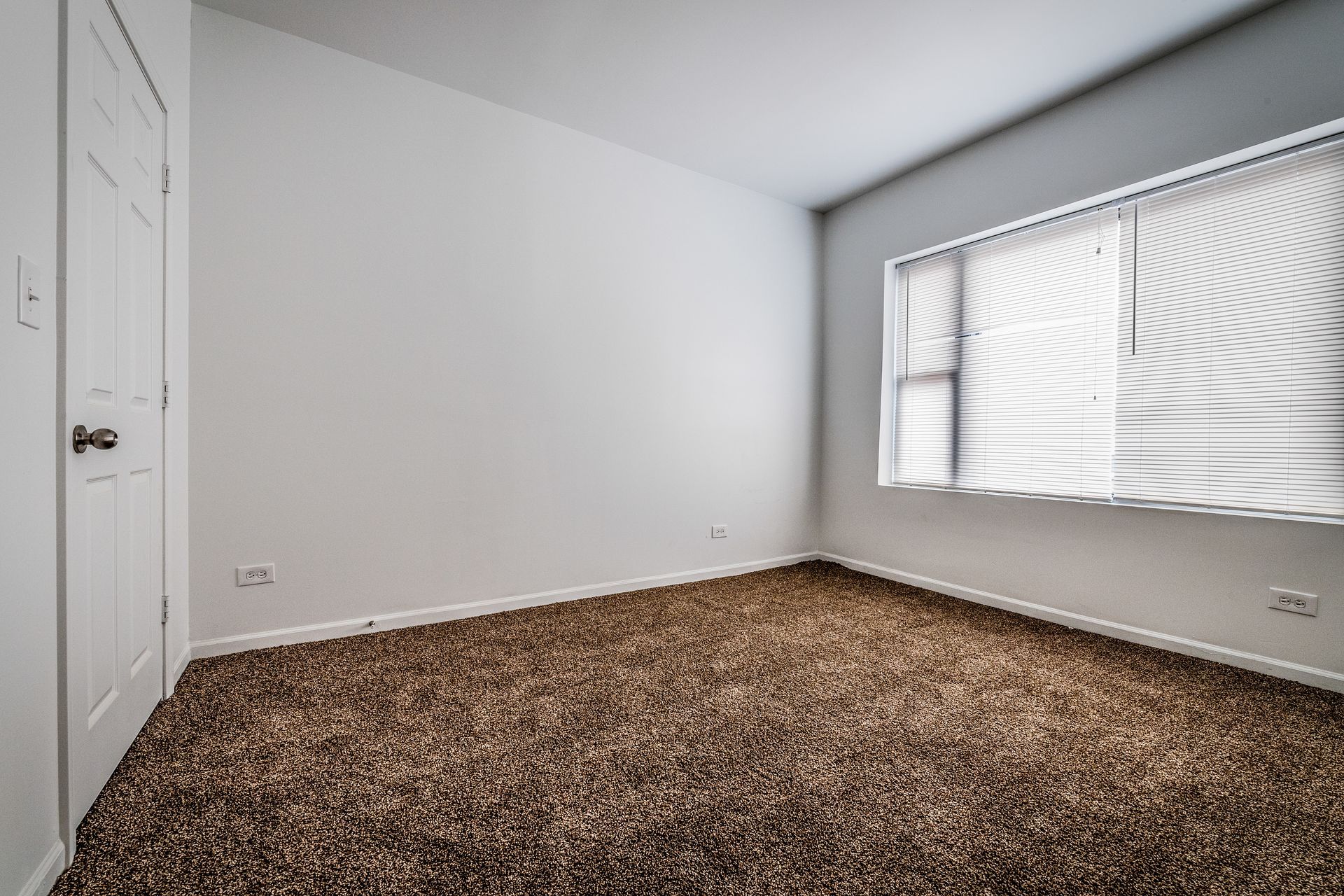 Empty room with brown carpet, white walls, and a window with blinds.