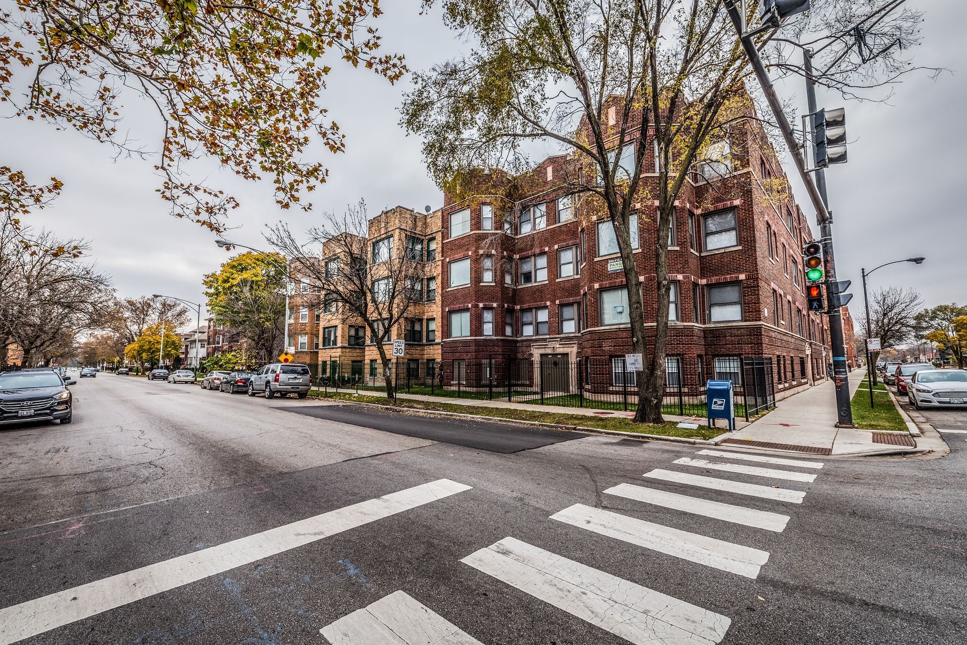 Apartment buildings on city street with crosswalk; overcast sky.