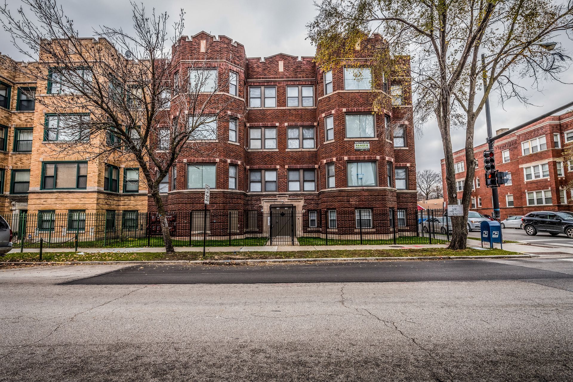 Red brick apartment building with architectural details; two adjacent buildings and street in front.