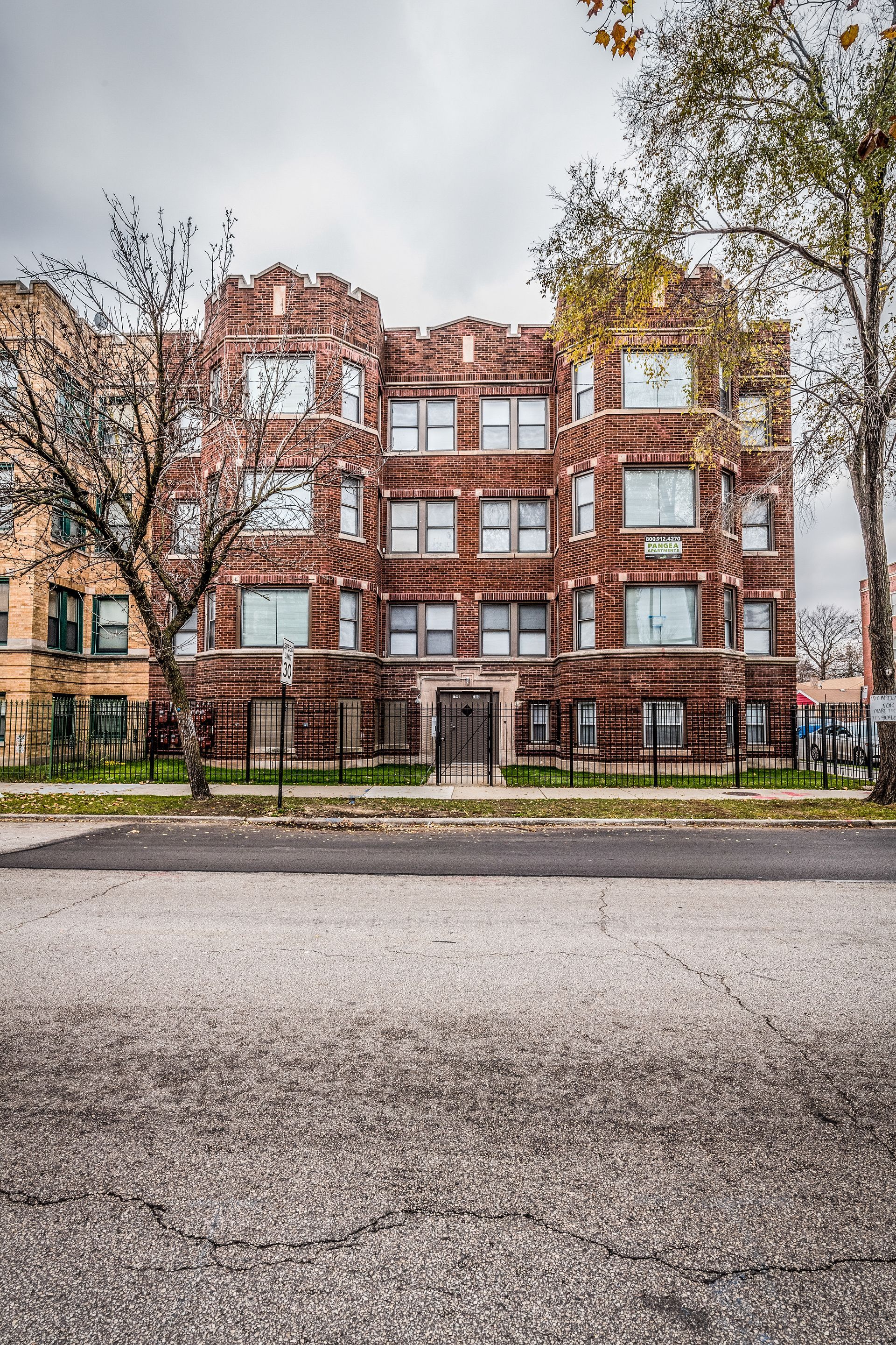 Brick apartment building with decorative turrets and windows, under a cloudy sky.