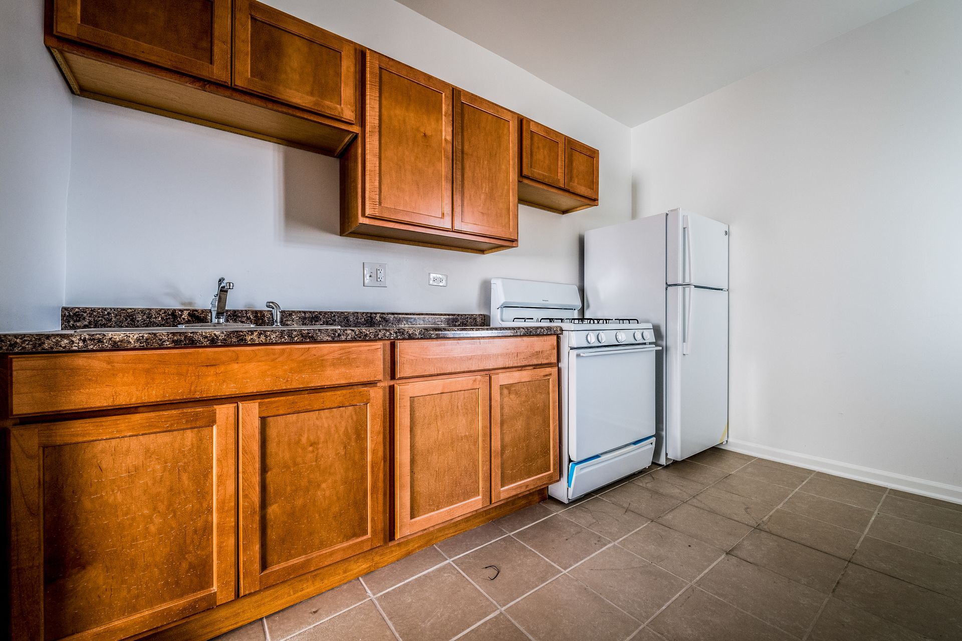 Kitchen with brown cabinets, white appliances, and speckled countertop.