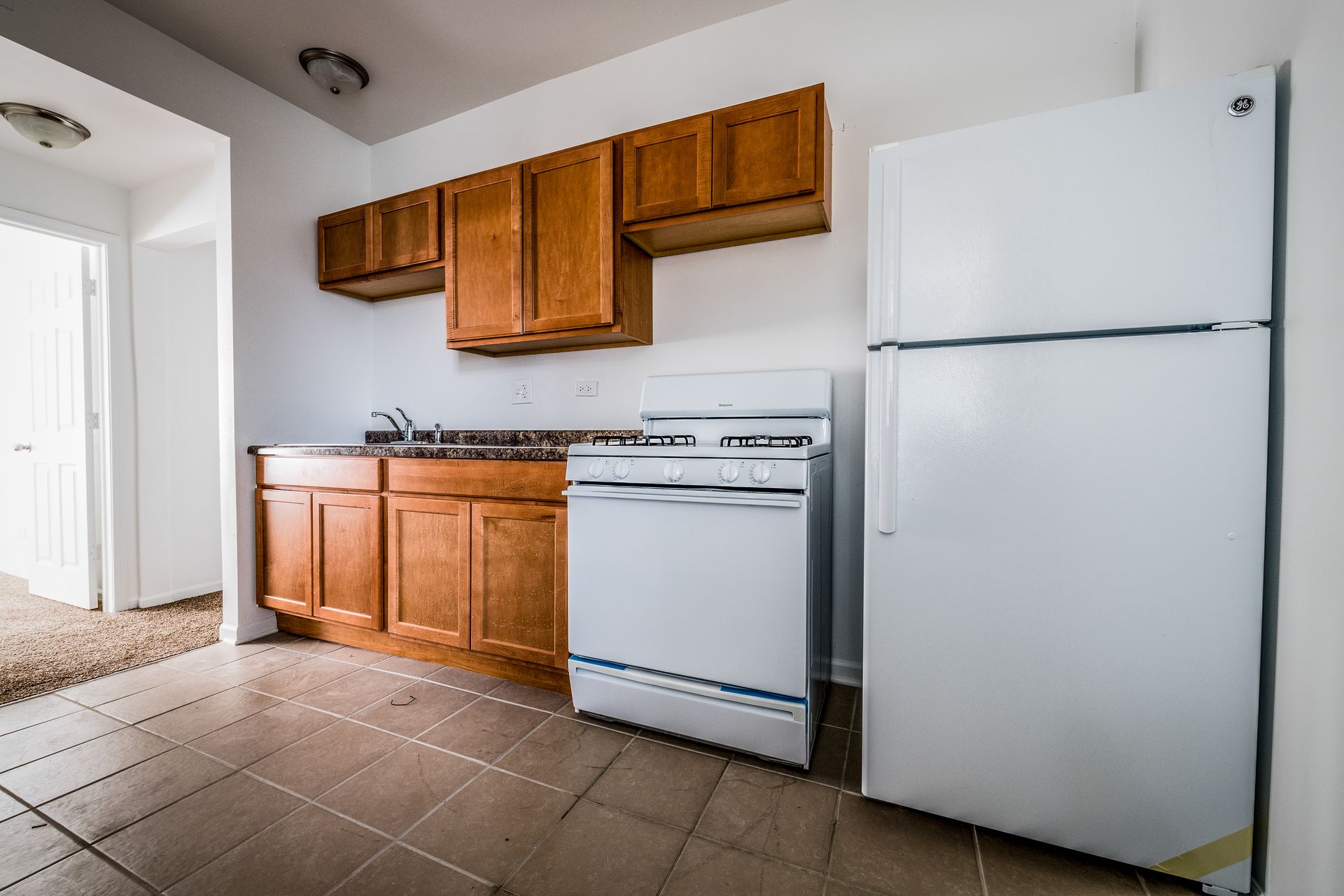 Kitchen with wooden cabinets, white appliances, and tile floor.