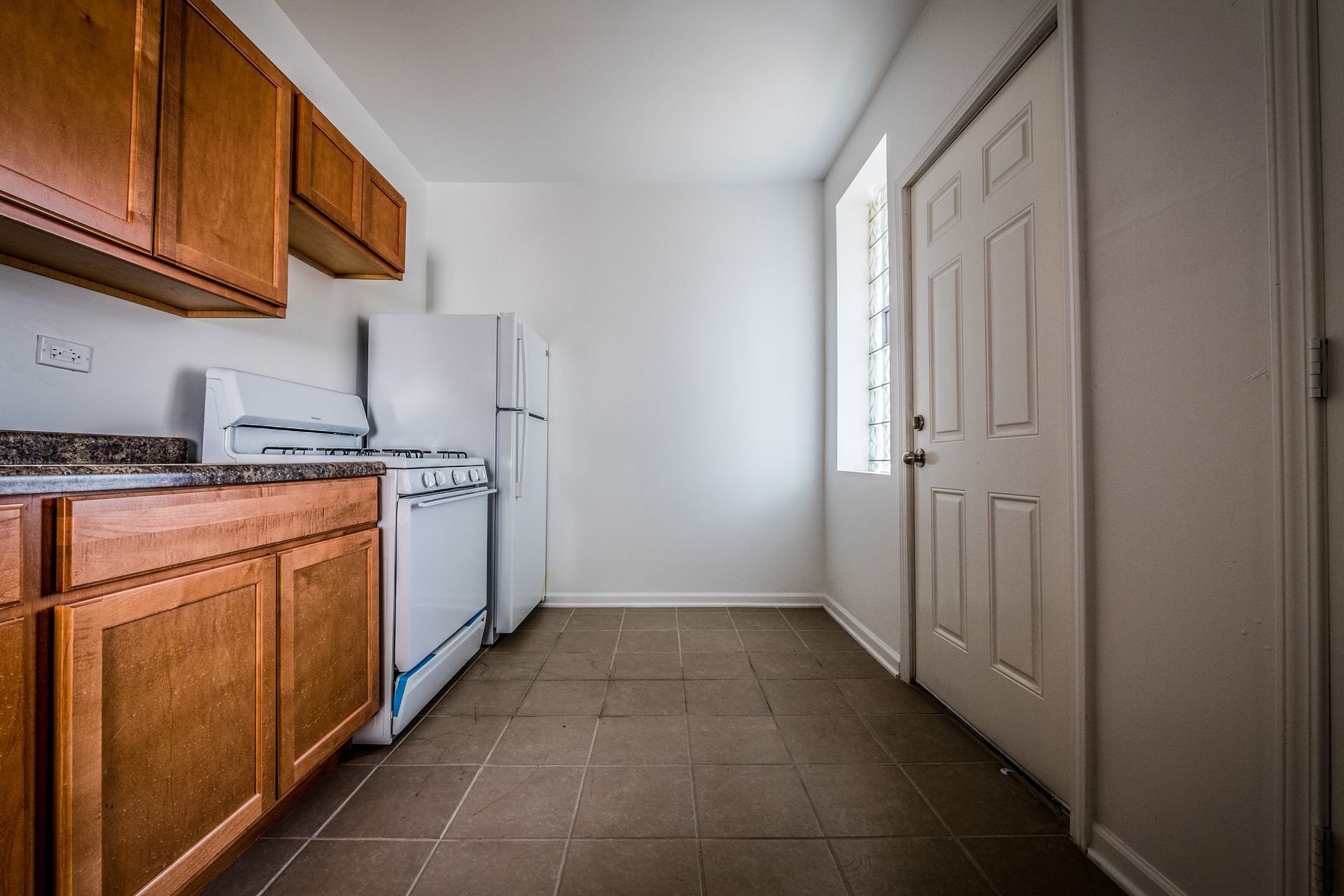 Kitchen with brown cabinets, white appliances, and a closed door.