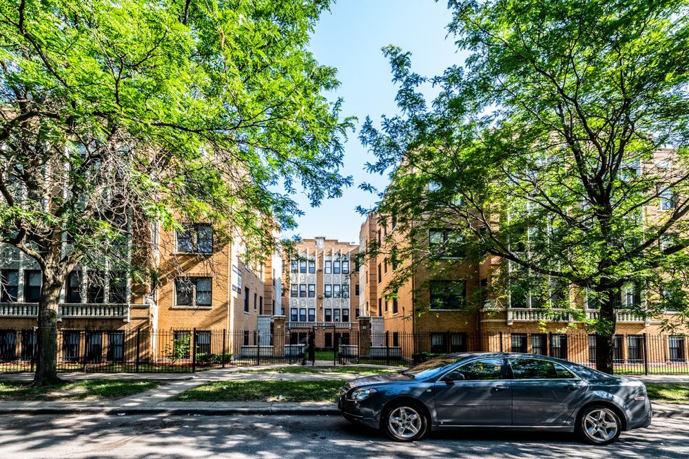 Row of brick apartment buildings with trees and a parked car.