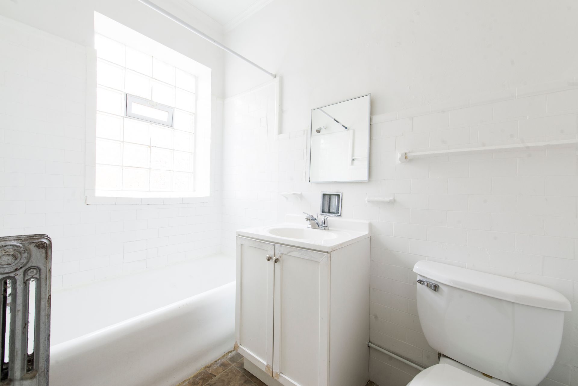 White bathroom with a bathtub, sink, toilet, window, and radiator.