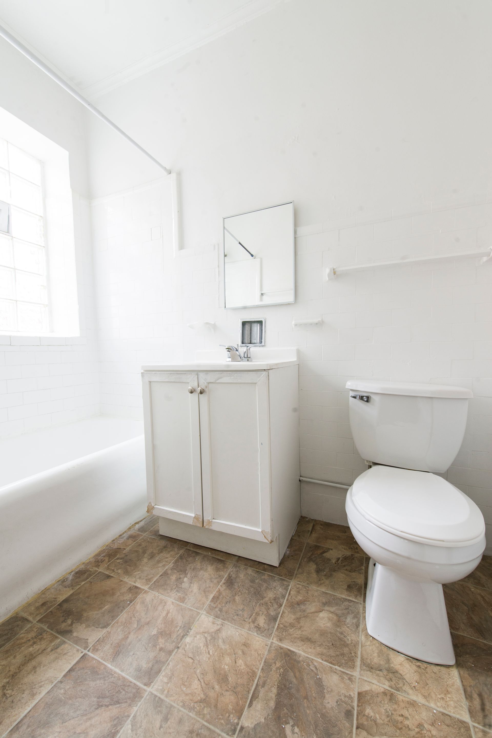 White bathroom with tub, sink, toilet, and brown tile floor.