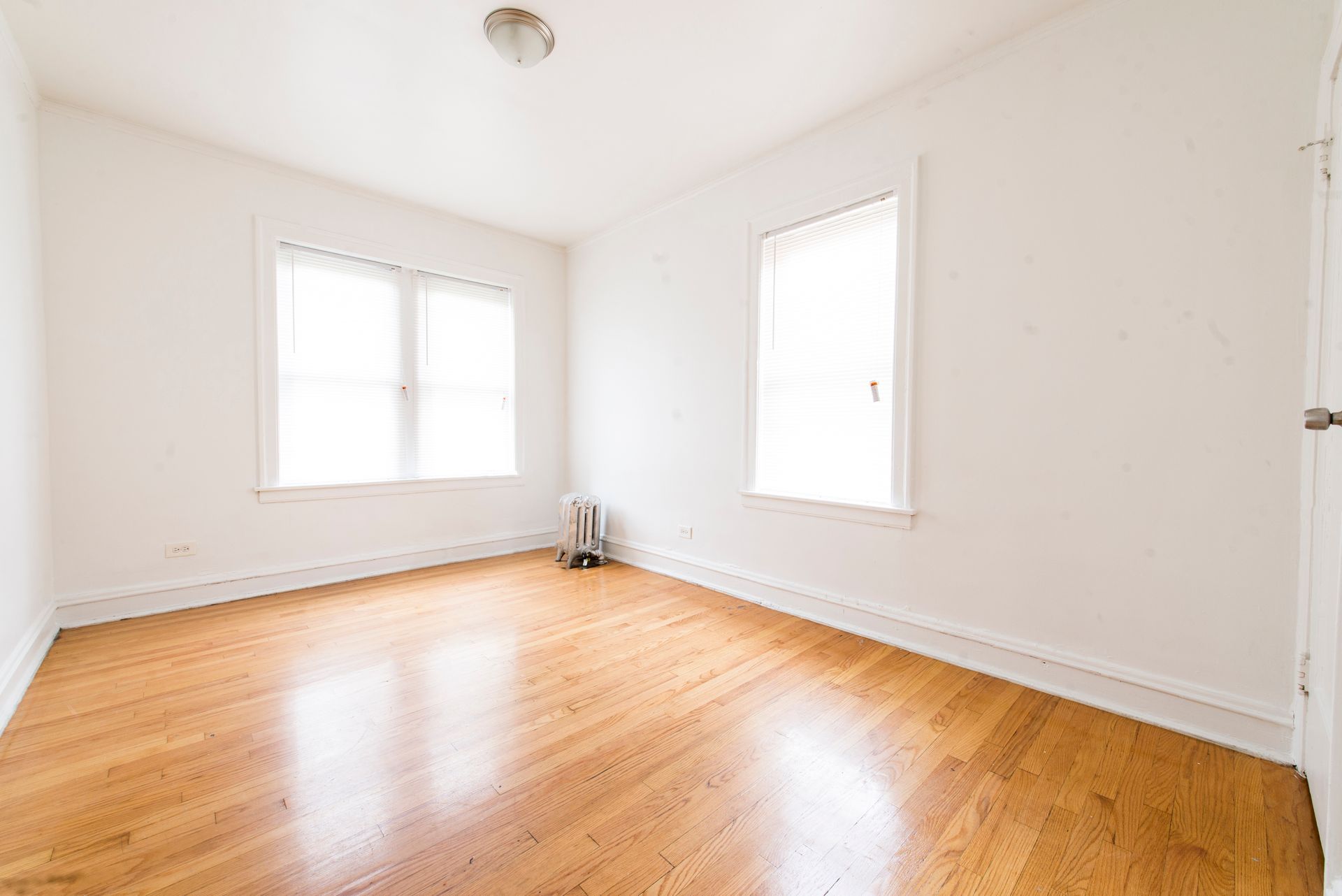 Empty room with hardwood floors, white walls, two windows, and a ceiling light.