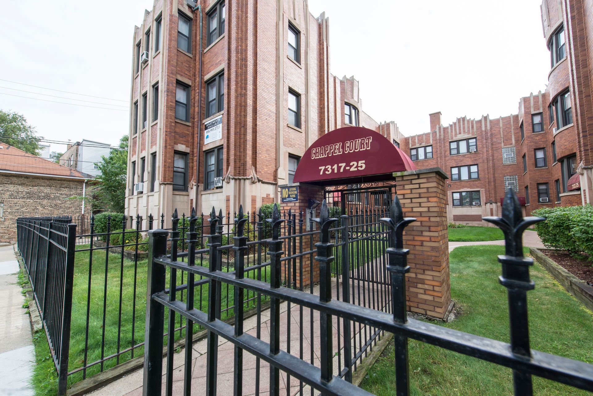 Brick apartment building with black wrought-iron fence and awning.