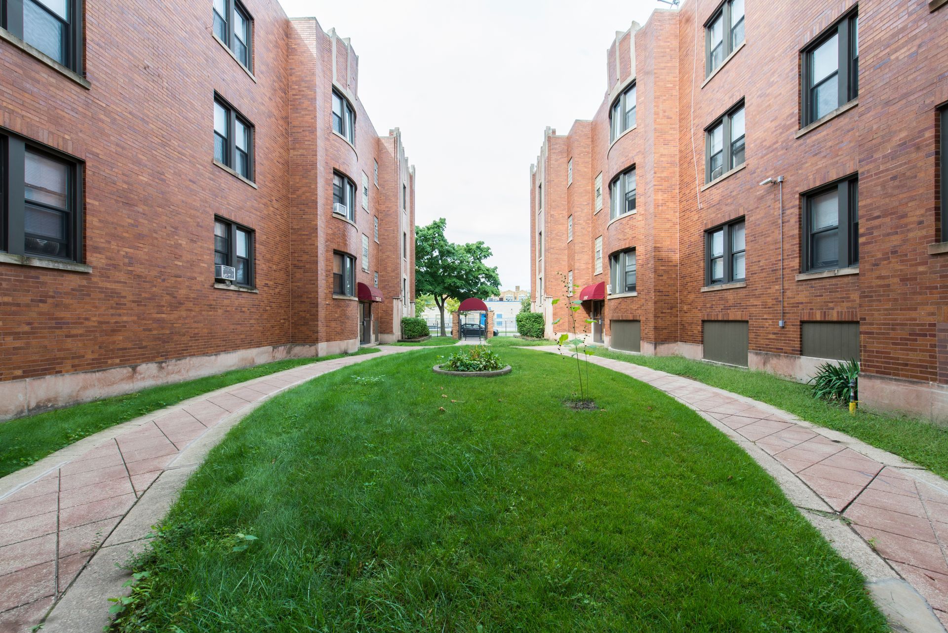 Two brick apartment buildings face each other, separated by a grassy lawn and walkways.