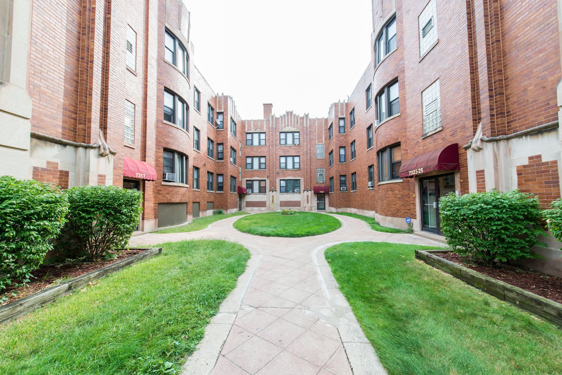 Courtyard between brick apartment buildings, pathways, and green lawn.