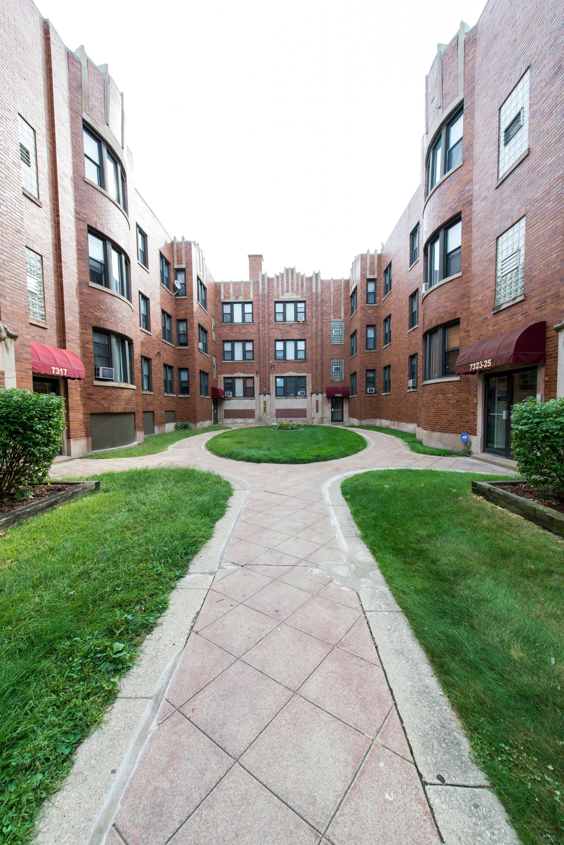 Brick apartment building courtyard with a green lawn and paved path.