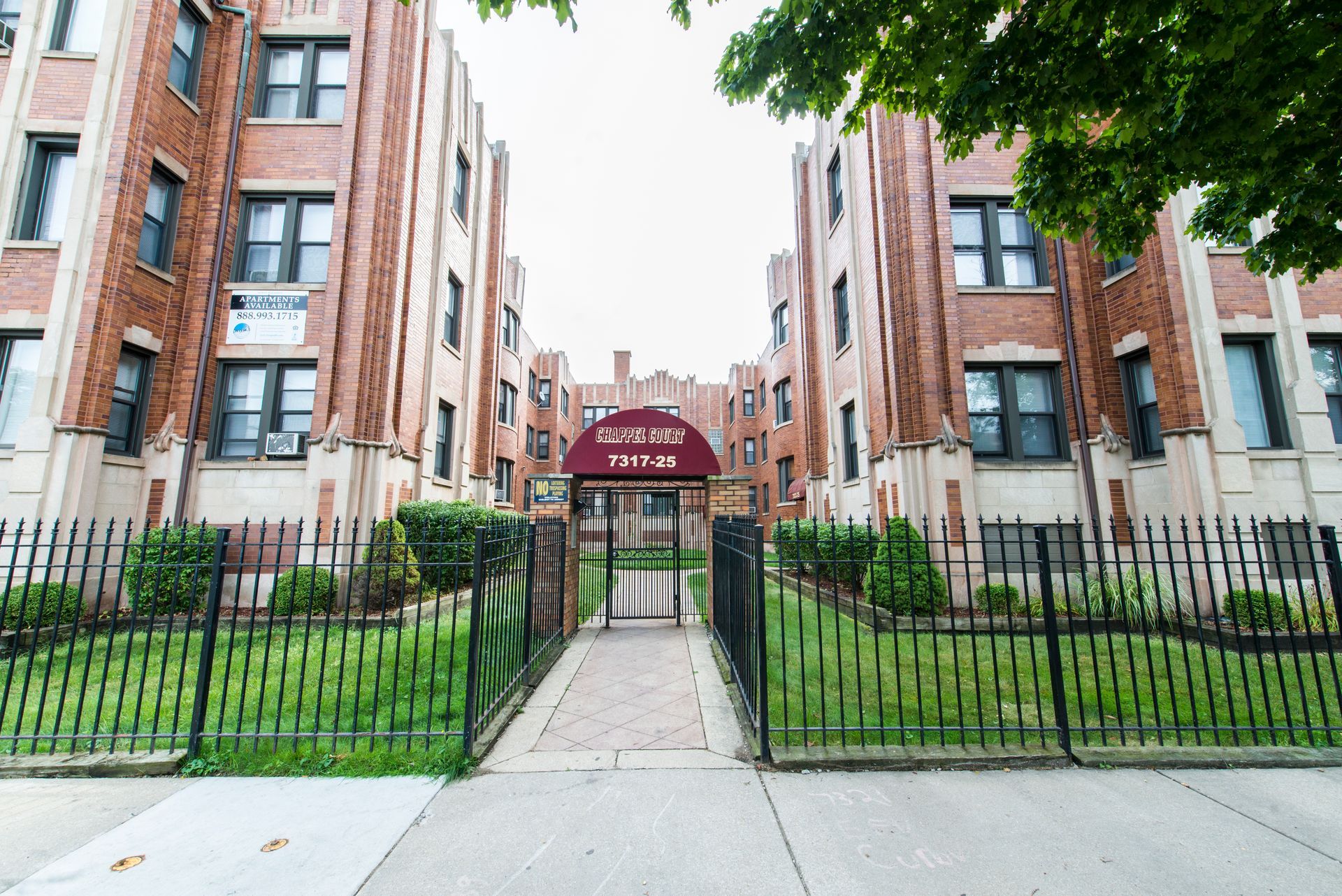 Brick apartment building with black fence and gated entrance. Sign reads 