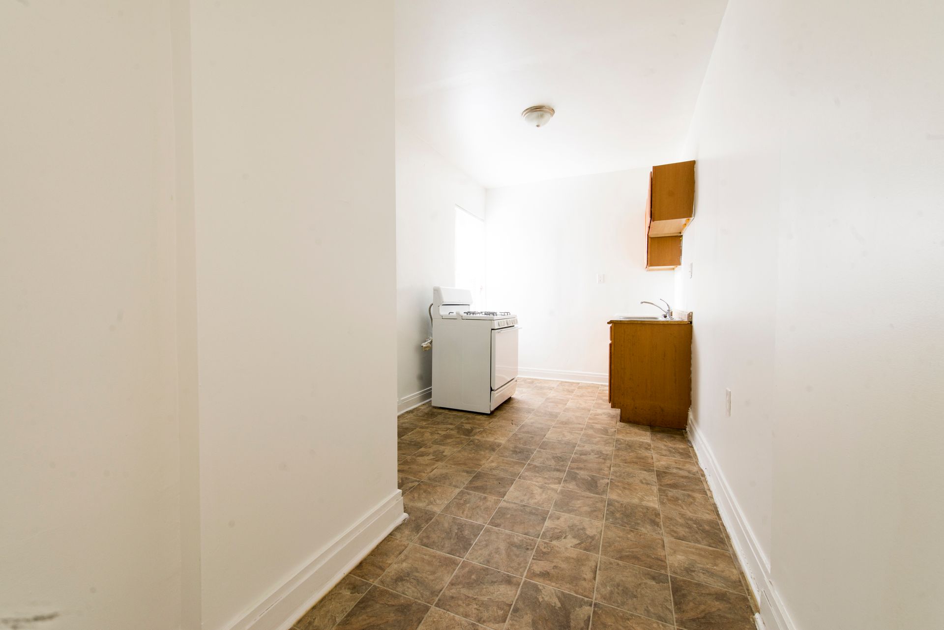 Empty kitchen with a stove, cabinets, and brown tiled floor.
