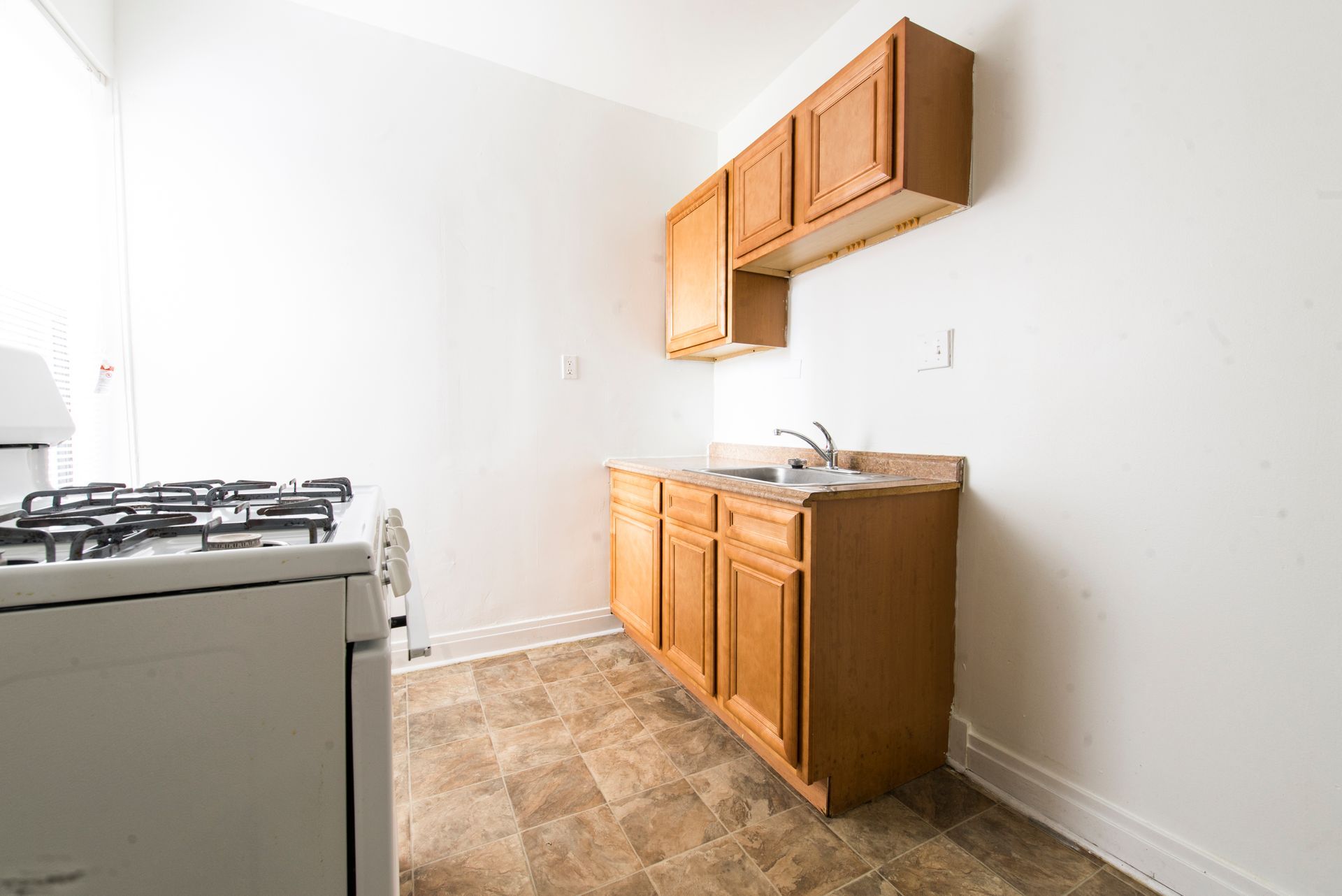 Kitchen with gas stove, cabinets, sink, and linoleum flooring.