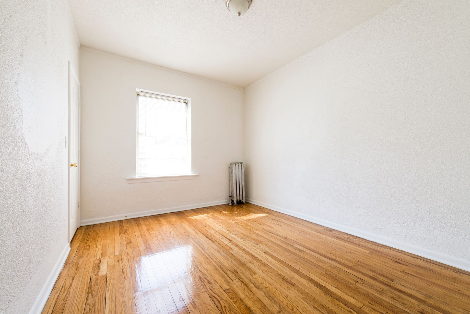 Empty room with wooden floor, white walls, and a window with natural light.