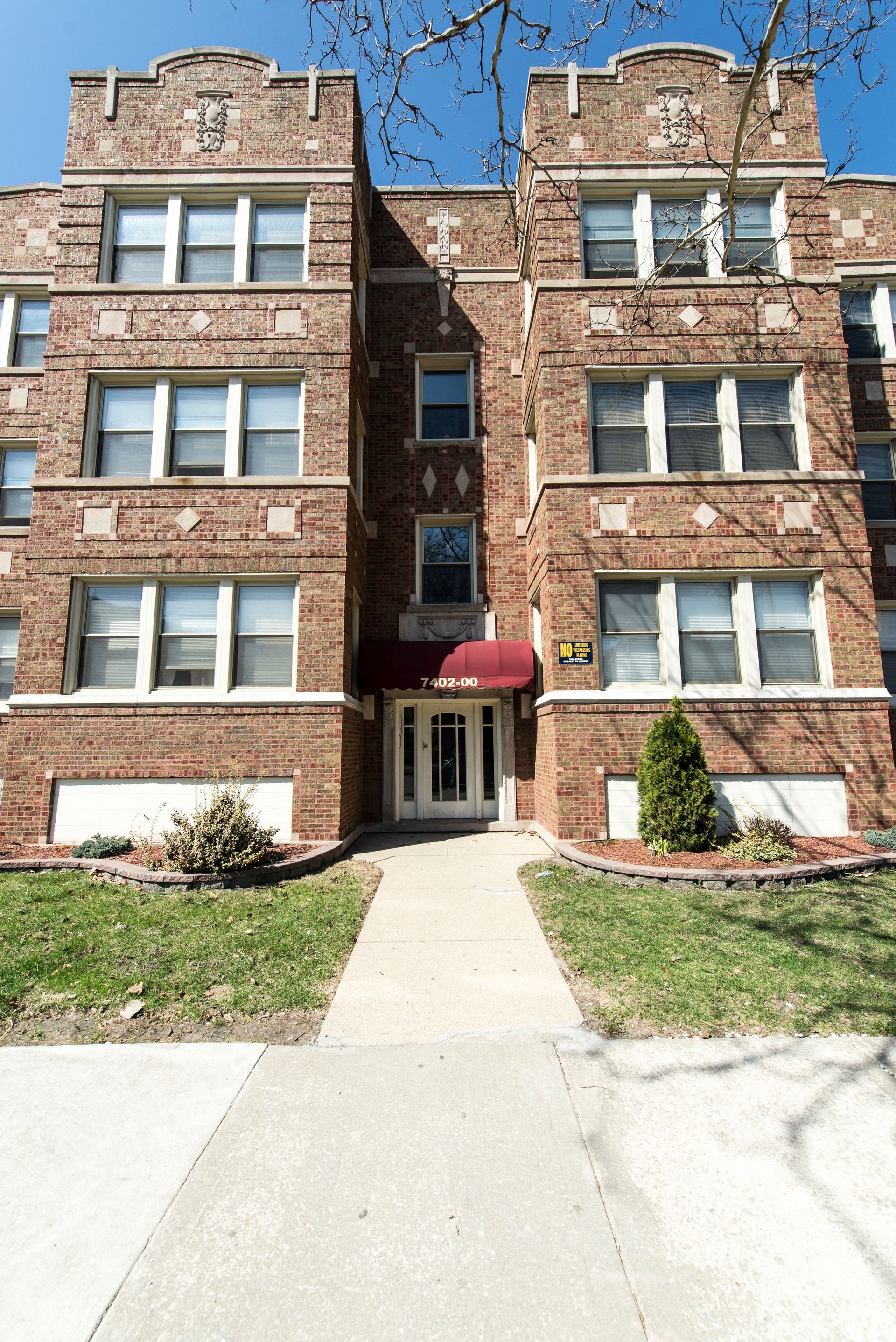 Brick apartment building with red awning over the front door and windows on multiple floors.