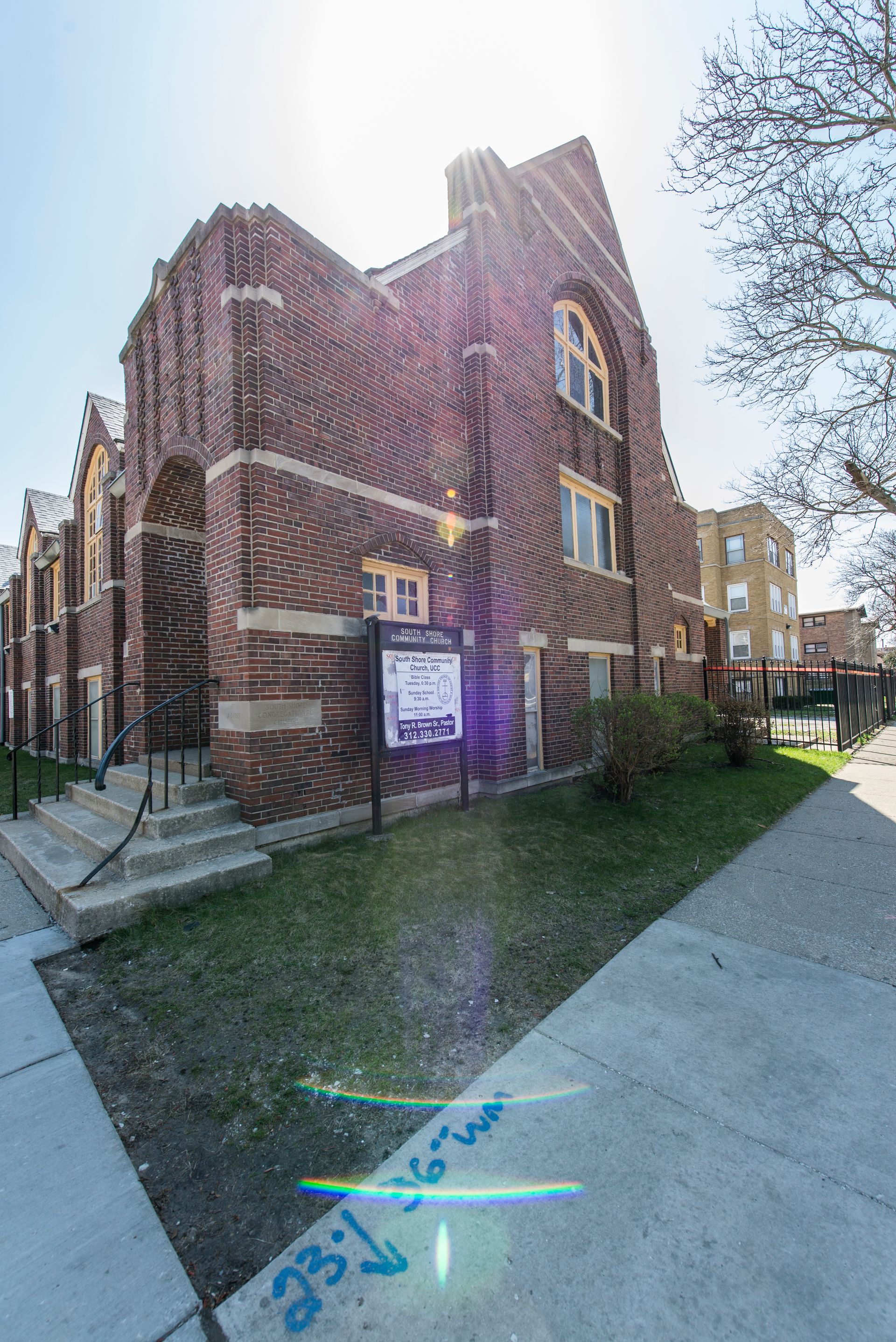 Brick church building with a sign on the front lawn, sunny day.