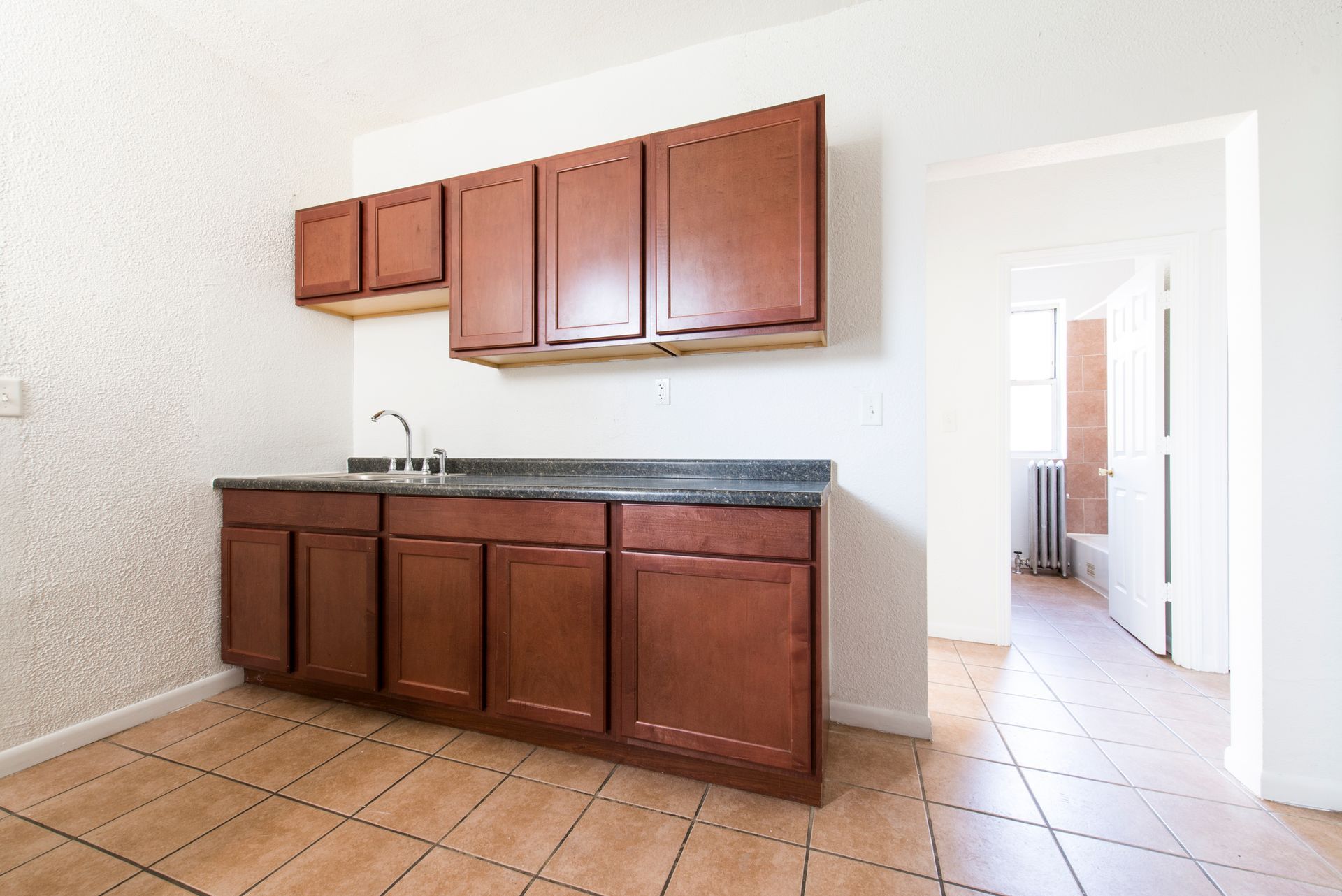 Kitchen with brown cabinets, gray countertop, sink, and tiled floor; door frame visible.