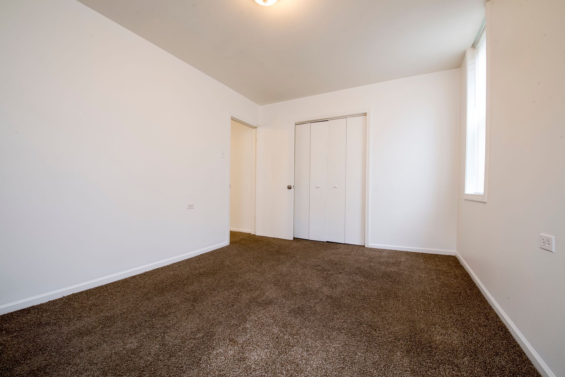 Empty room with brown carpet, white walls, closet, and a small window.
