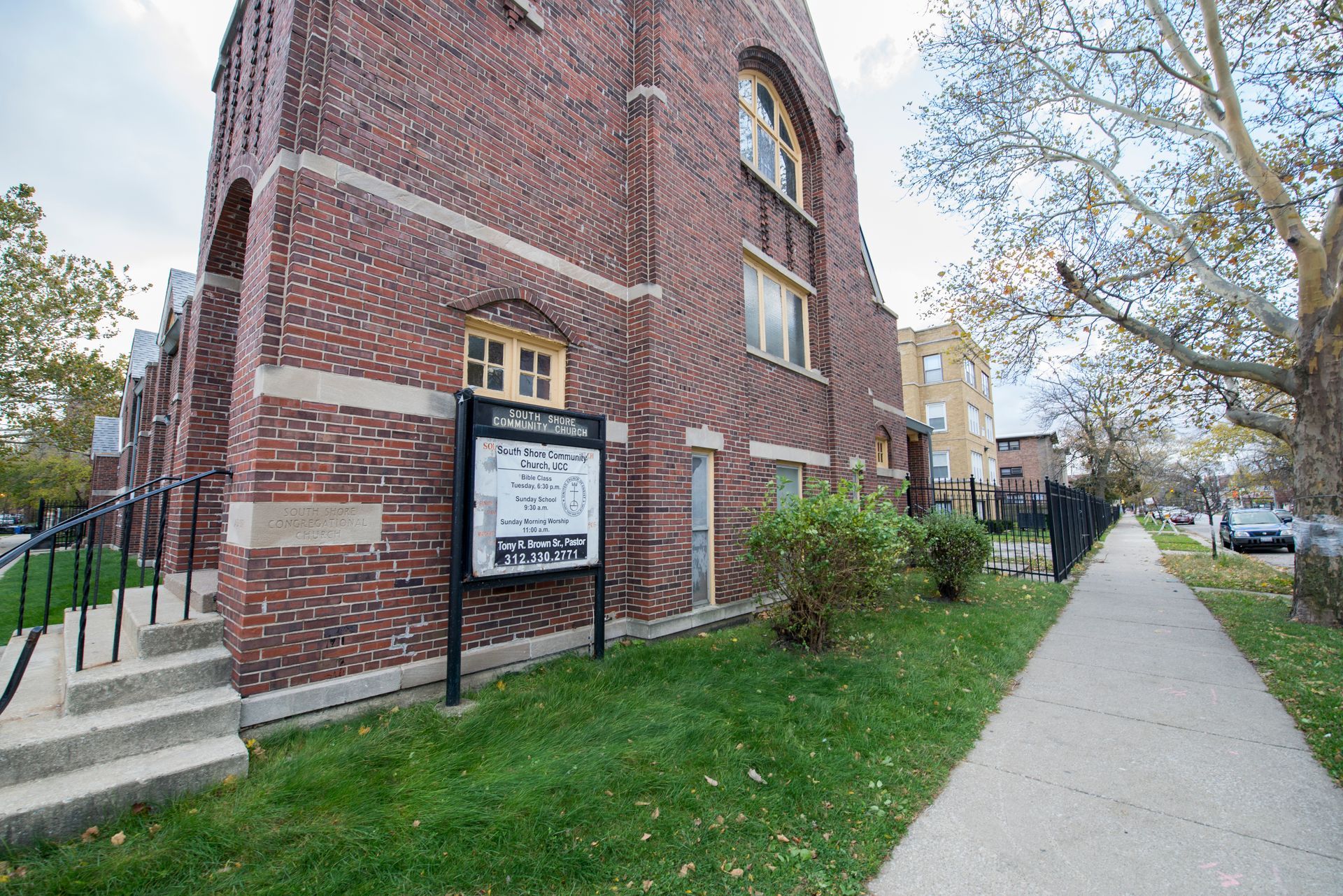 Brick church building with a sign on the lawn, sidewalk on the right.