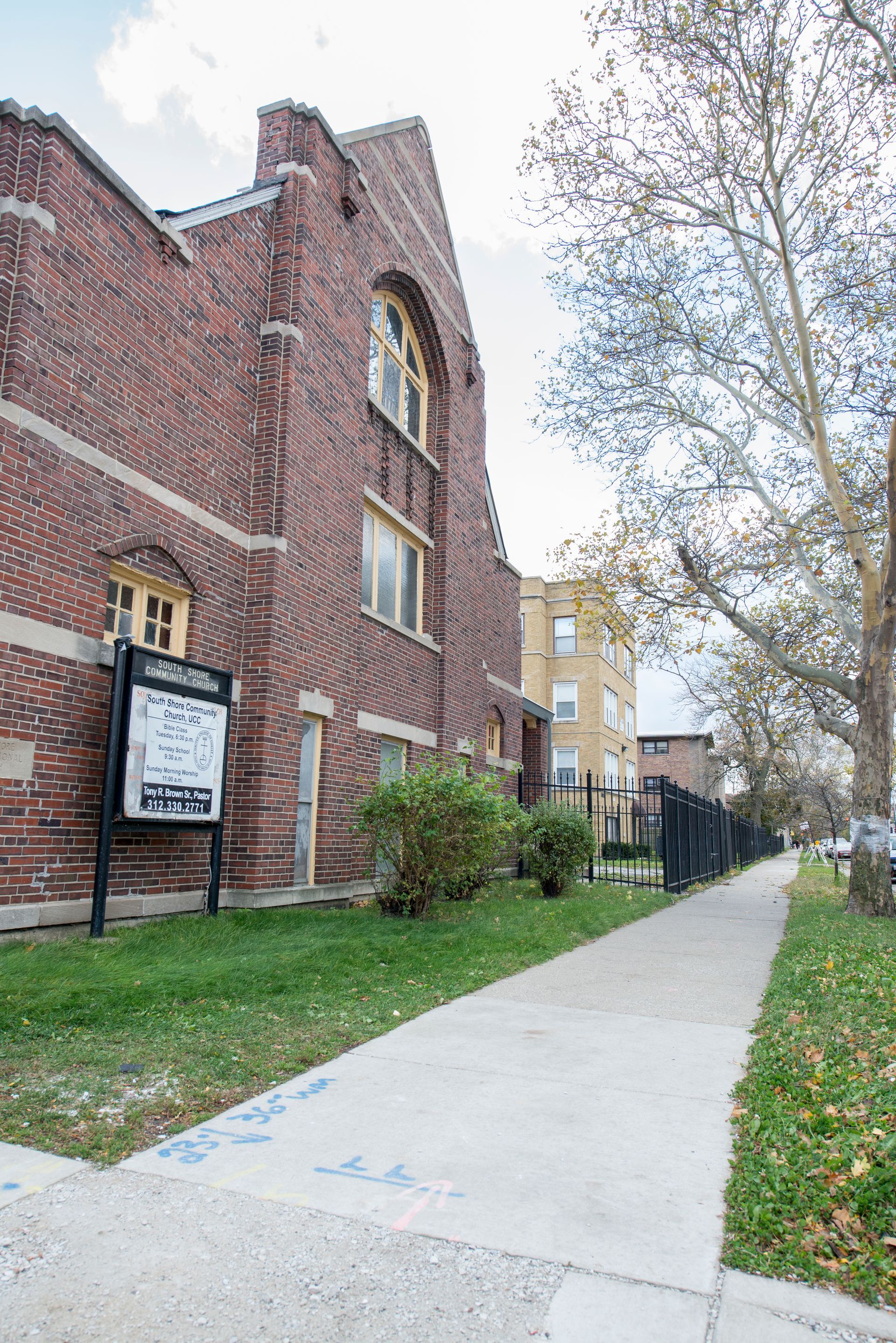 Brick church building with a sidewalk, grassy area, and trees.
