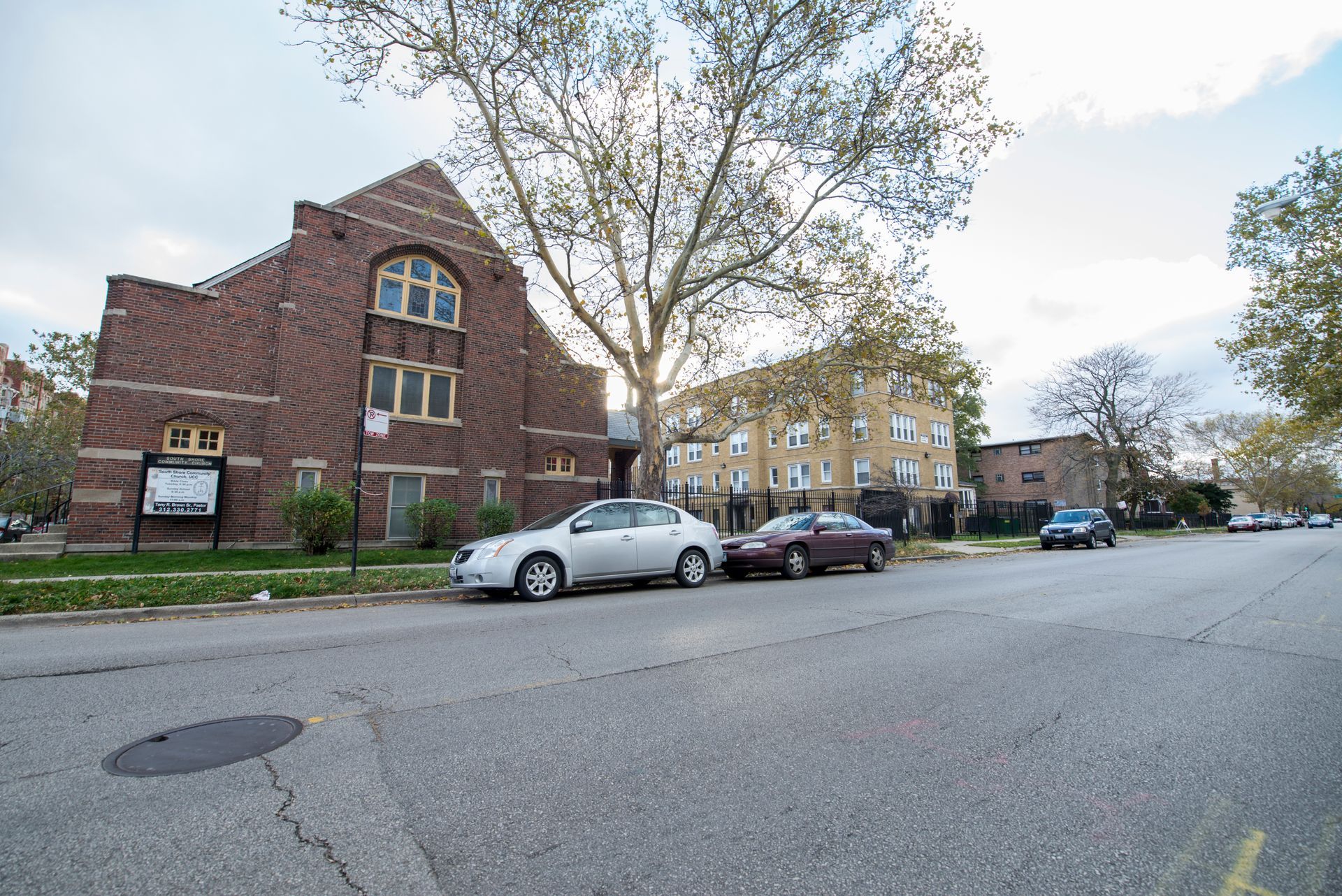 Brick church and apartment building on a street with parked cars. Overcast sky.