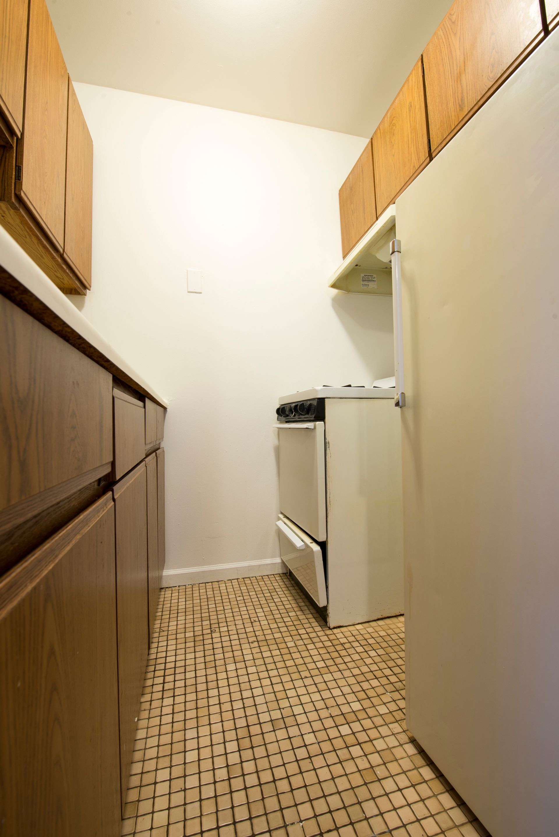 Narrow kitchen with cabinets, stove, refrigerator, and tile floor.