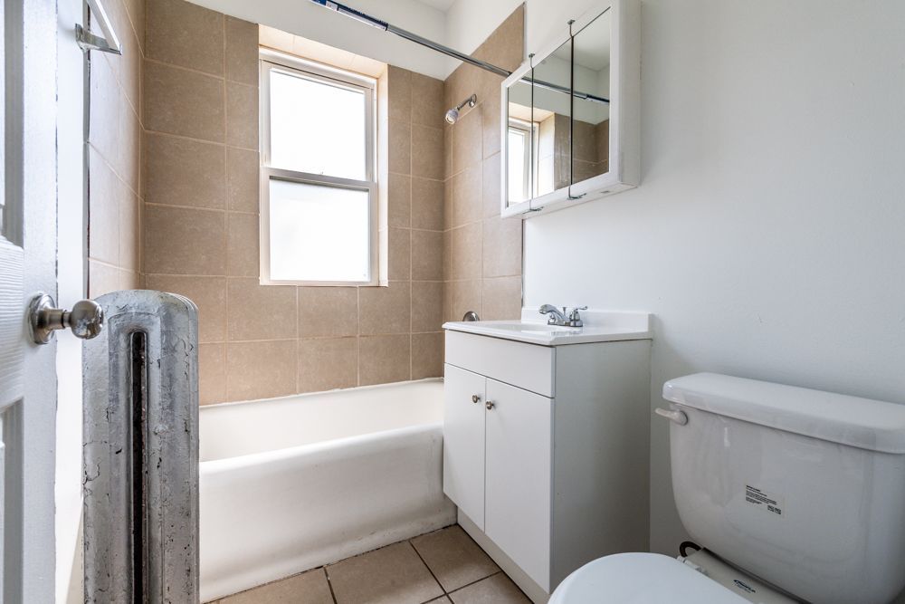 Bathroom with white fixtures, beige tiled wall, and window.