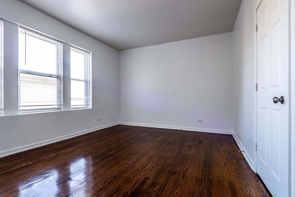 Empty room with hardwood floors, white walls, two windows, and a closed white door.