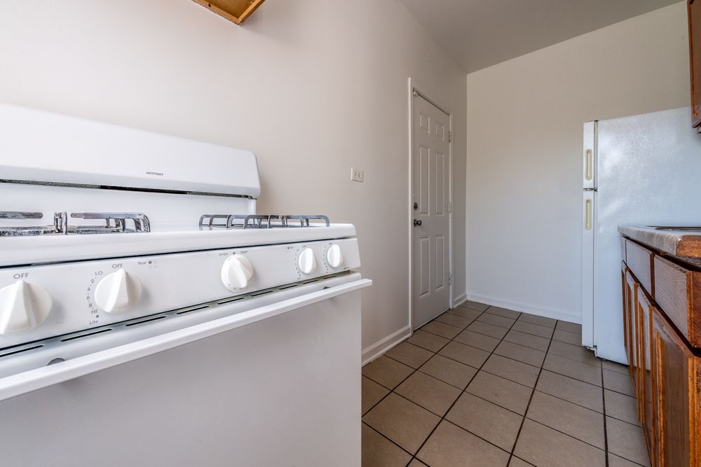White kitchen with stove, refrigerator, cabinets, and a door, likely in a rental unit.