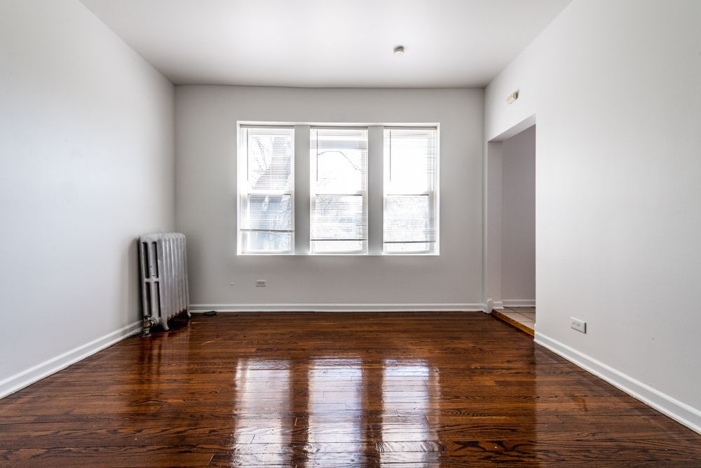 Empty room with wood floors, radiator, window, doorway, and white walls.