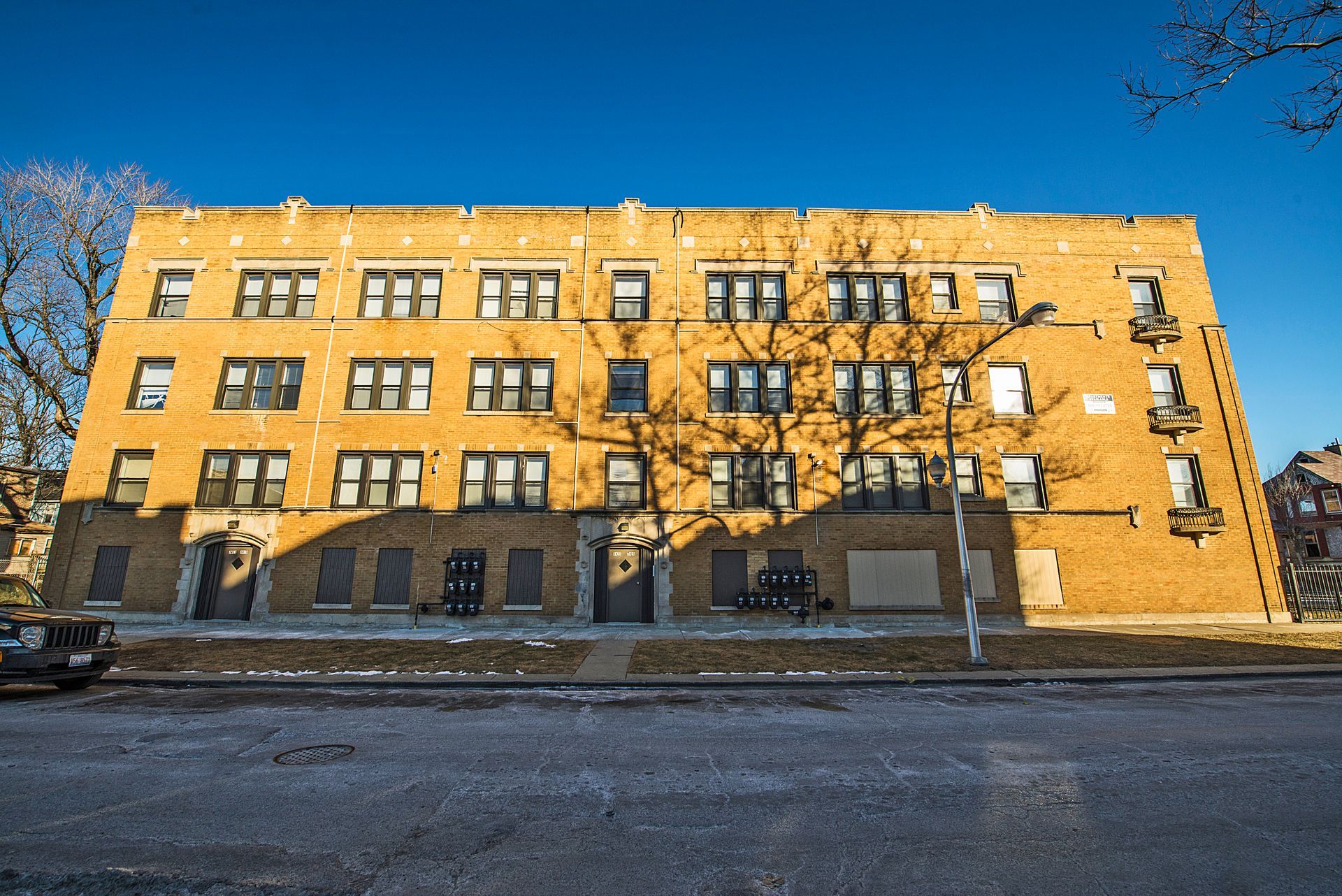 Yellow brick apartment building with boarded-up ground floor windows under a clear blue sky.