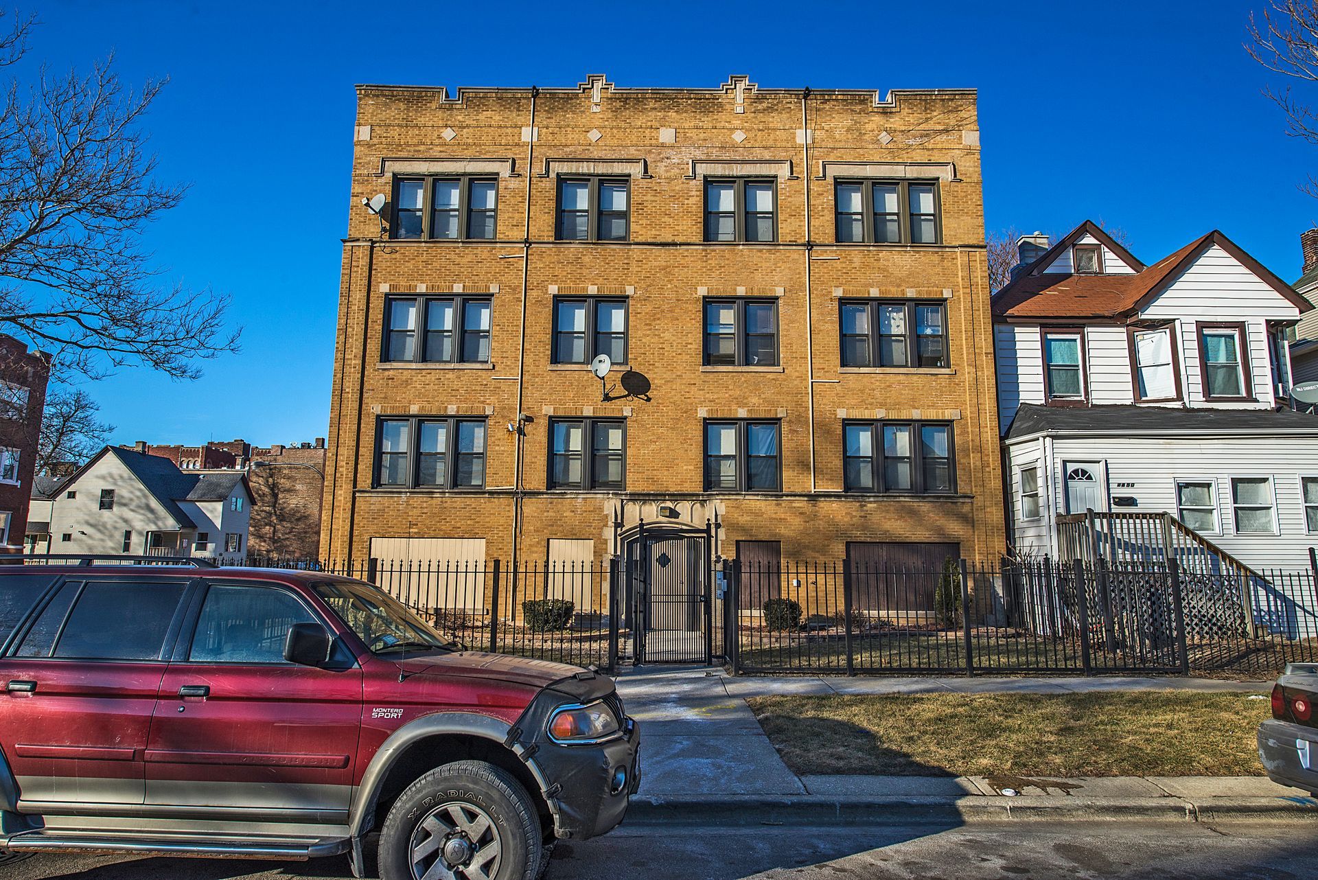 Brick apartment building with red SUV parked in front on a sunny day.