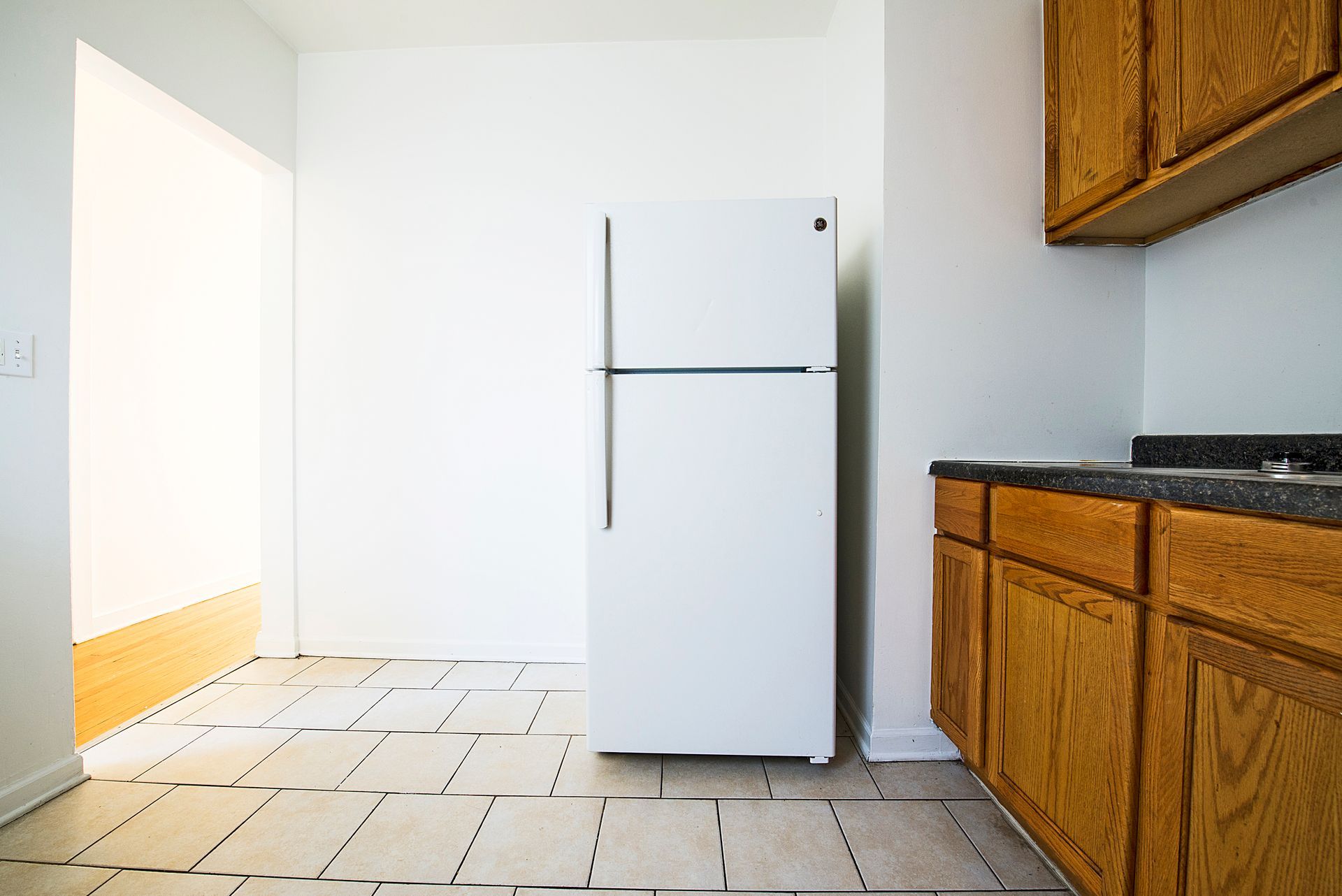 Kitchen with white refrigerator, wood cabinets, and tiled floor.