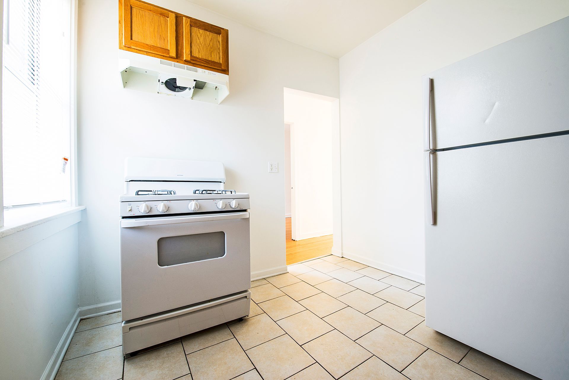 White kitchen with a stove, refrigerator, cabinets, and tiled floor.