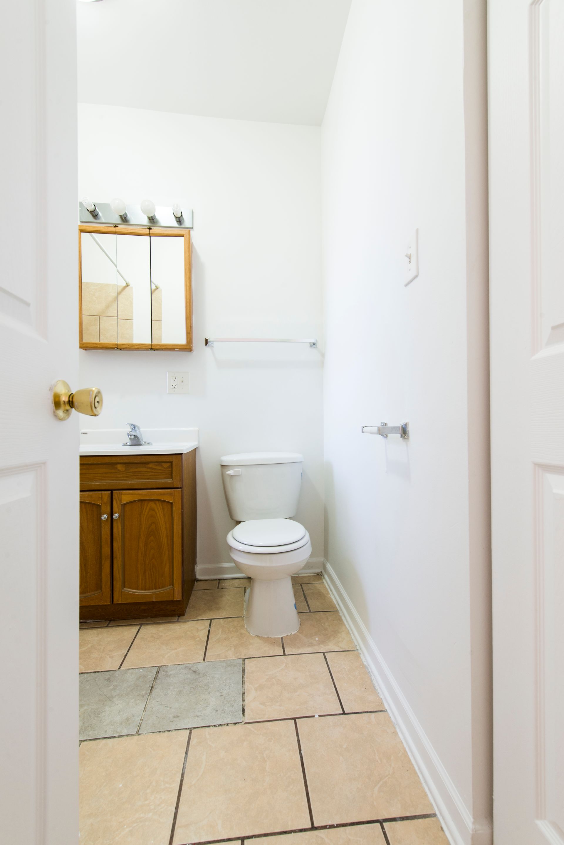 Small bathroom with toilet, vanity, mirror, and tan tiled floor.